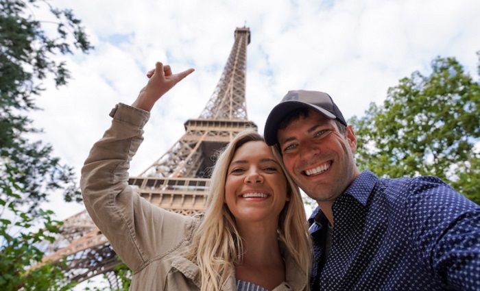 happy couple in front of the Eiffel Tower on an eiffel tower climbing tour pointing to the summit 