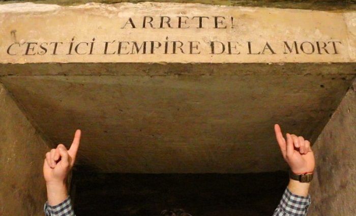 Paris Catacombs visitor pointing to a sign that reads “Stop, This Is Death’s Empire”