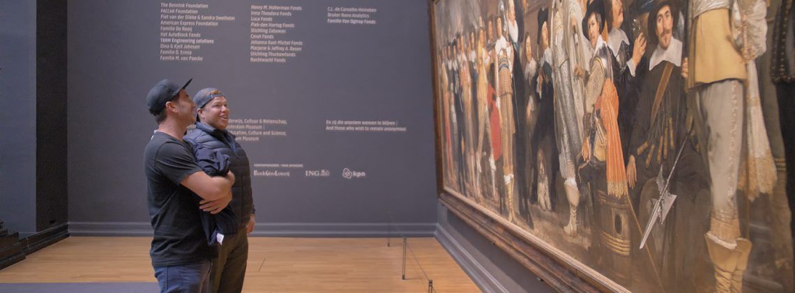 Two men standing in front of a painting.