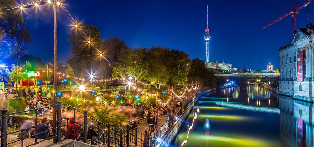 Berlin Canal at night next to a colorful restaurant with many people.