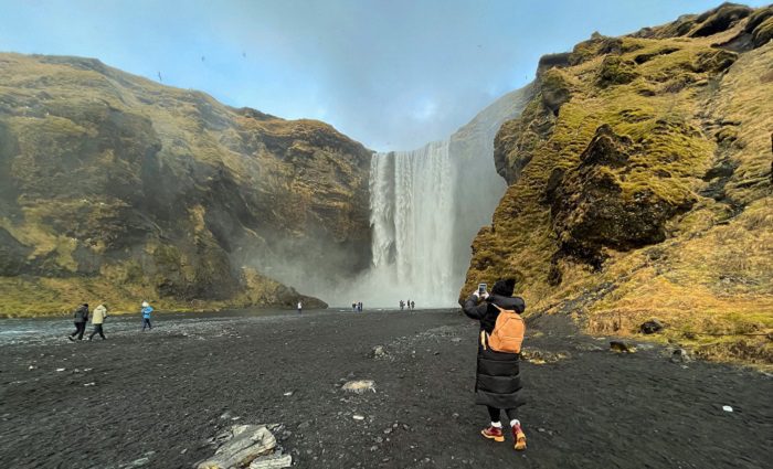 woman taking picture of skogafoss waterfall