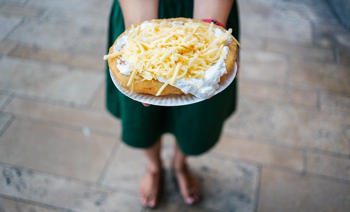 young woman holding traditional Langos food with cheese and sour cream topping