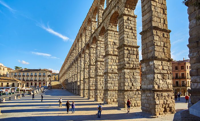 Side view of the Aqueduct of Segovia in the Plaza Azoguejo with people walking beneath the arches.