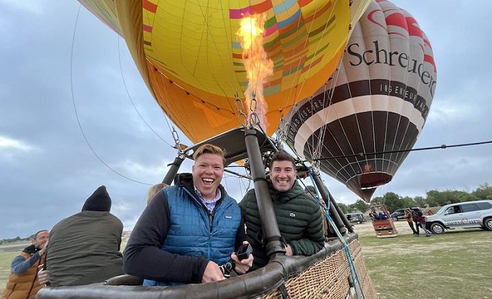 Two people smiling in the basket of a hot air balloon getting ready to enjoy the views of Segovia and the Aqueduct in a hot air balloon ride.