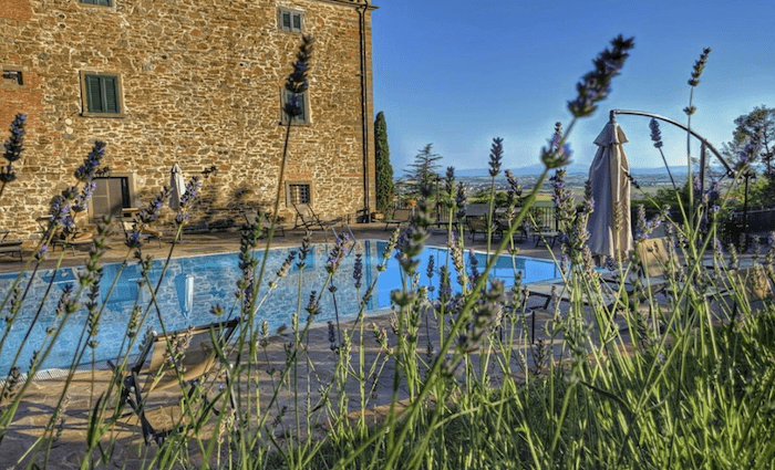 A view through the lavender of the pool area with the stone villa and Arezzo countryside in the background.   