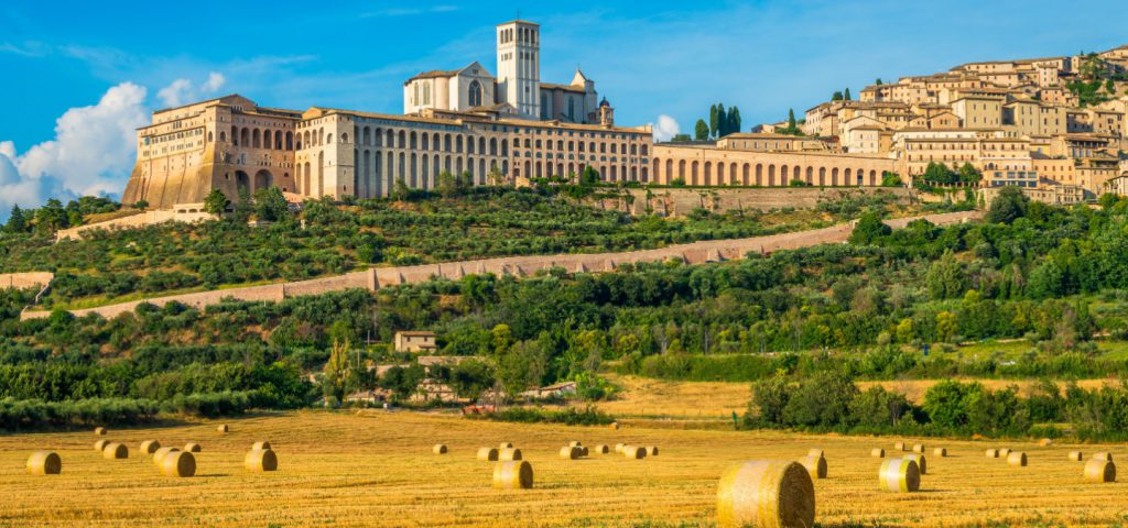 Autumn panorama of Assisi on a sunny day, perched above the surrounding countryside with bales of hay in the fields below