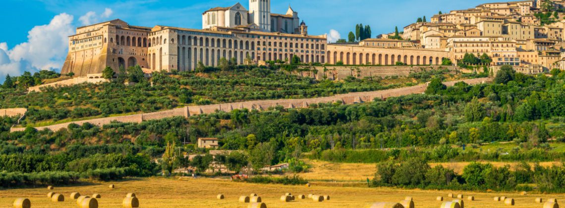 Autumn panorama of Assisi on a sunny day, perched above the surrounding countryside with bales of hay in the fields below