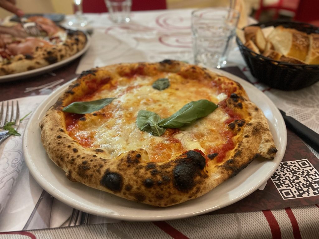 Pizza on a plate topped with a basil leaf.