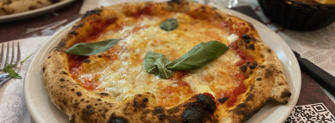 Pizza on a plate topped with a basil leaf.