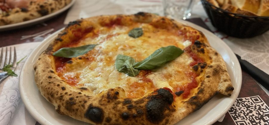 Pizza on a plate topped with a basil leaf.