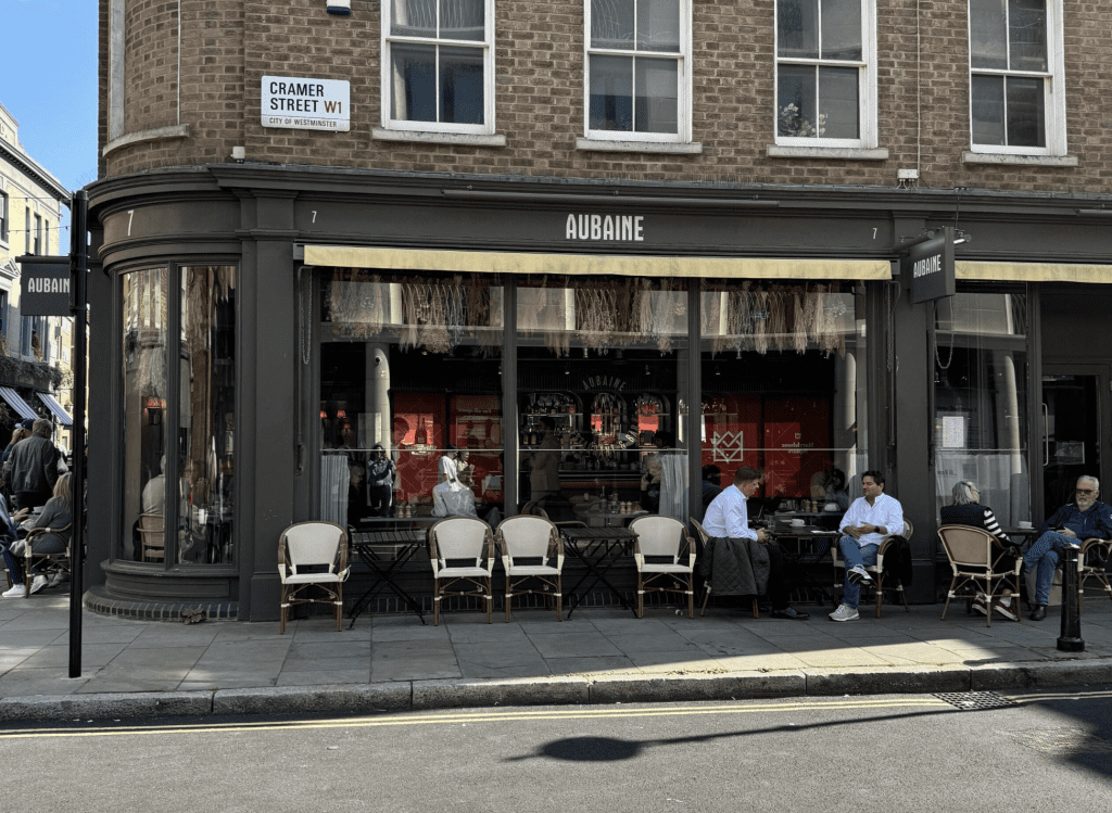 Cafe with people sitting in front in white chairs.