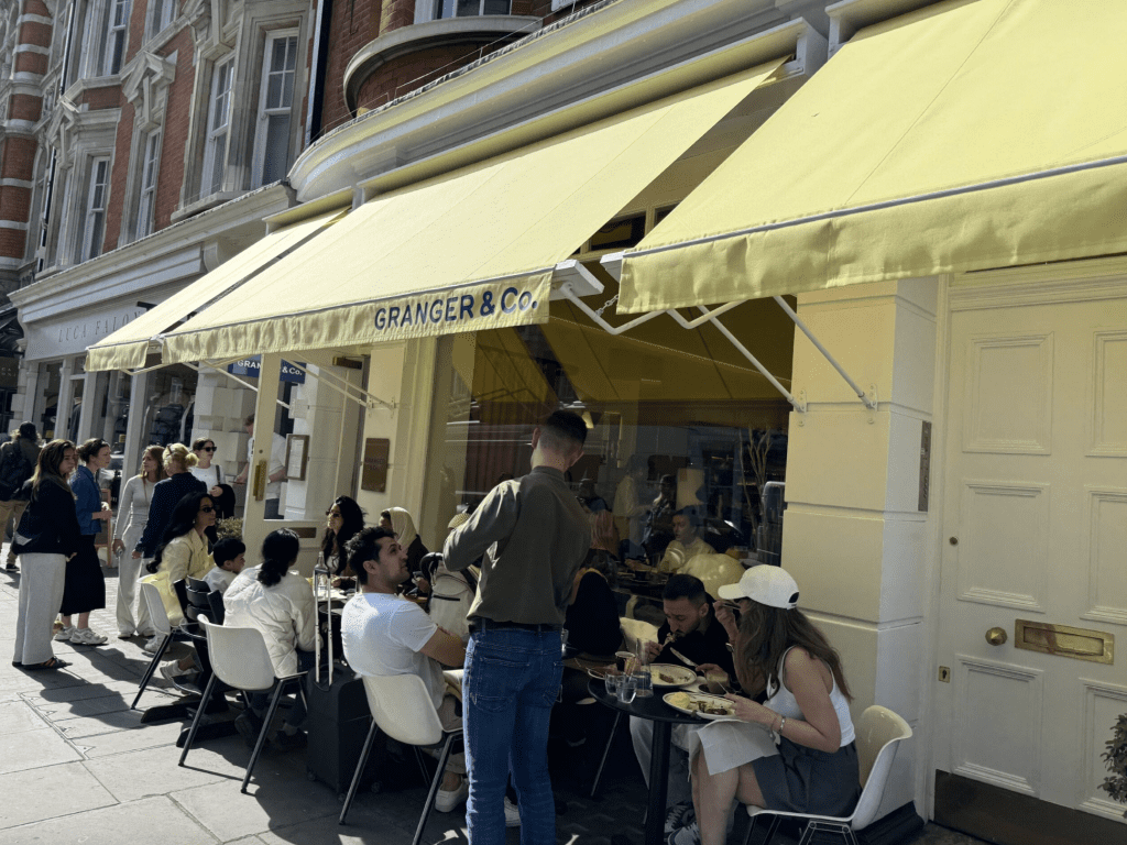 People sitting at tables in front of a yellow cafe awning.