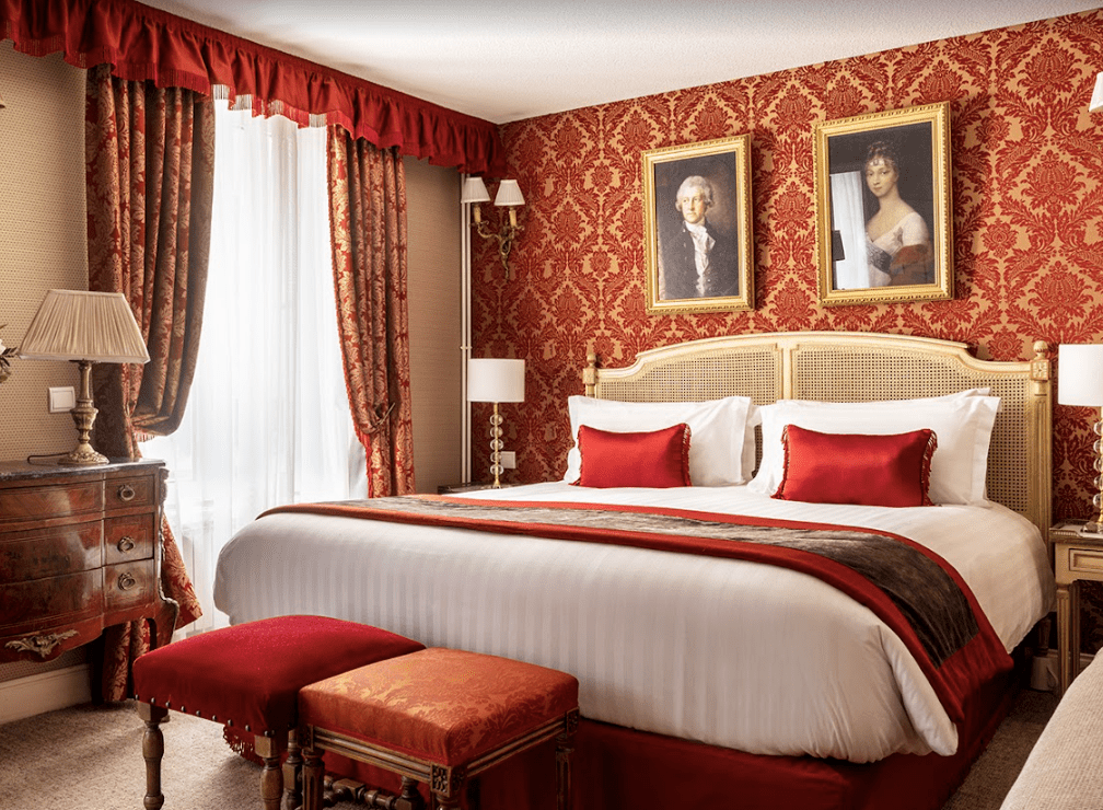 Red and gold wallpaper with antique oil paintings hanging on the wall.