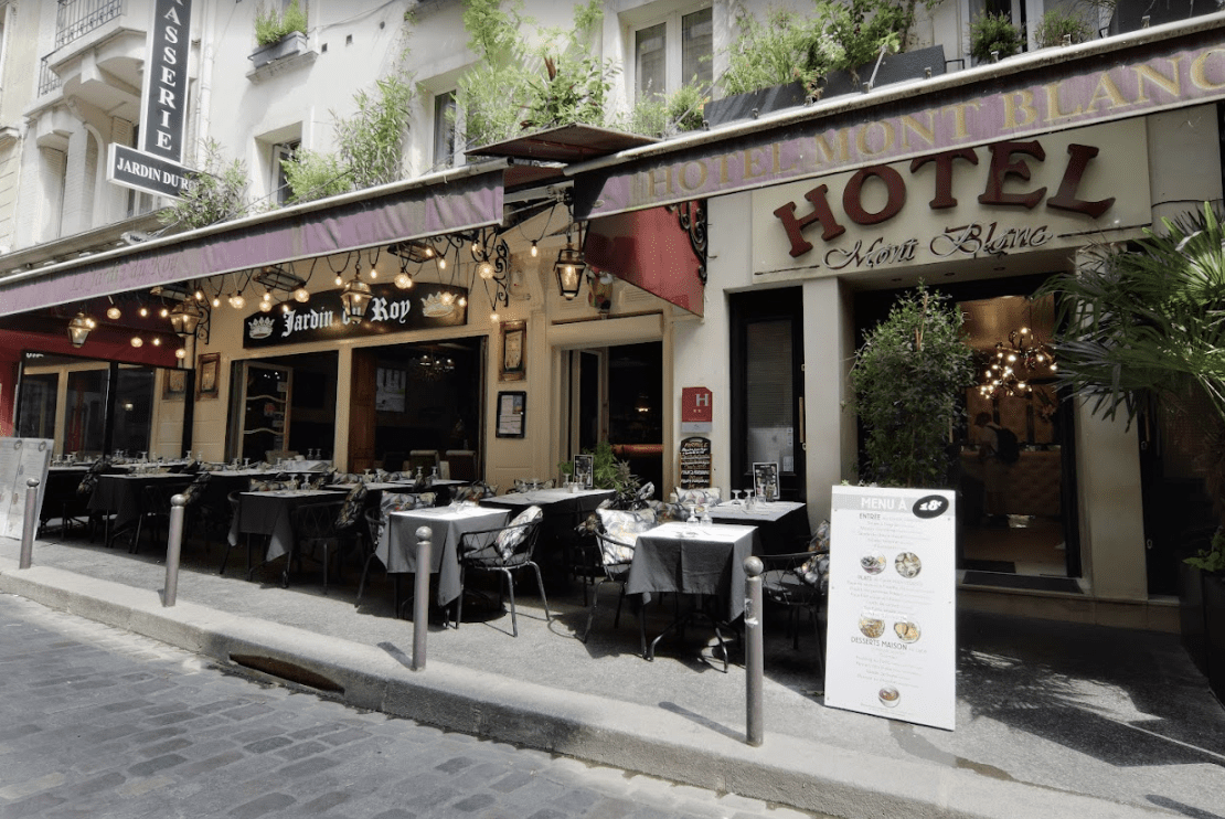 White building with red awnings and wooden dining tables.