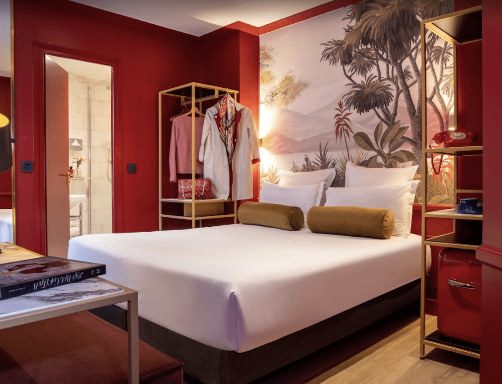 A White bed with red walls and green velvet pillows.