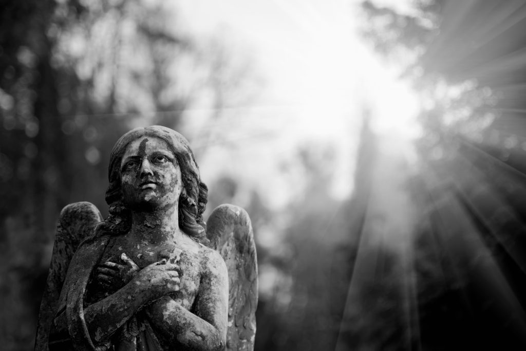 A black and white photo of a stone cemetery angel.