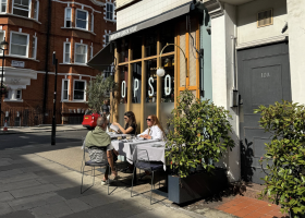 People eating at dining tables in front of a London Cafe.