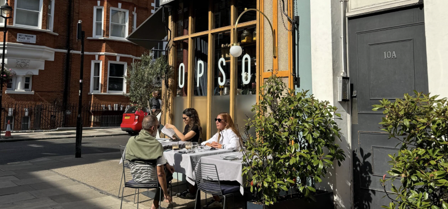 People eating at dining tables in front of a London Cafe.