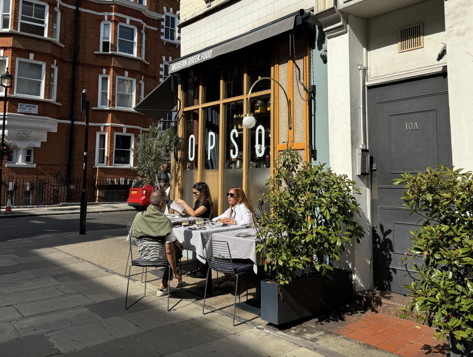 People eating at dining tables in front of a London Cafe.