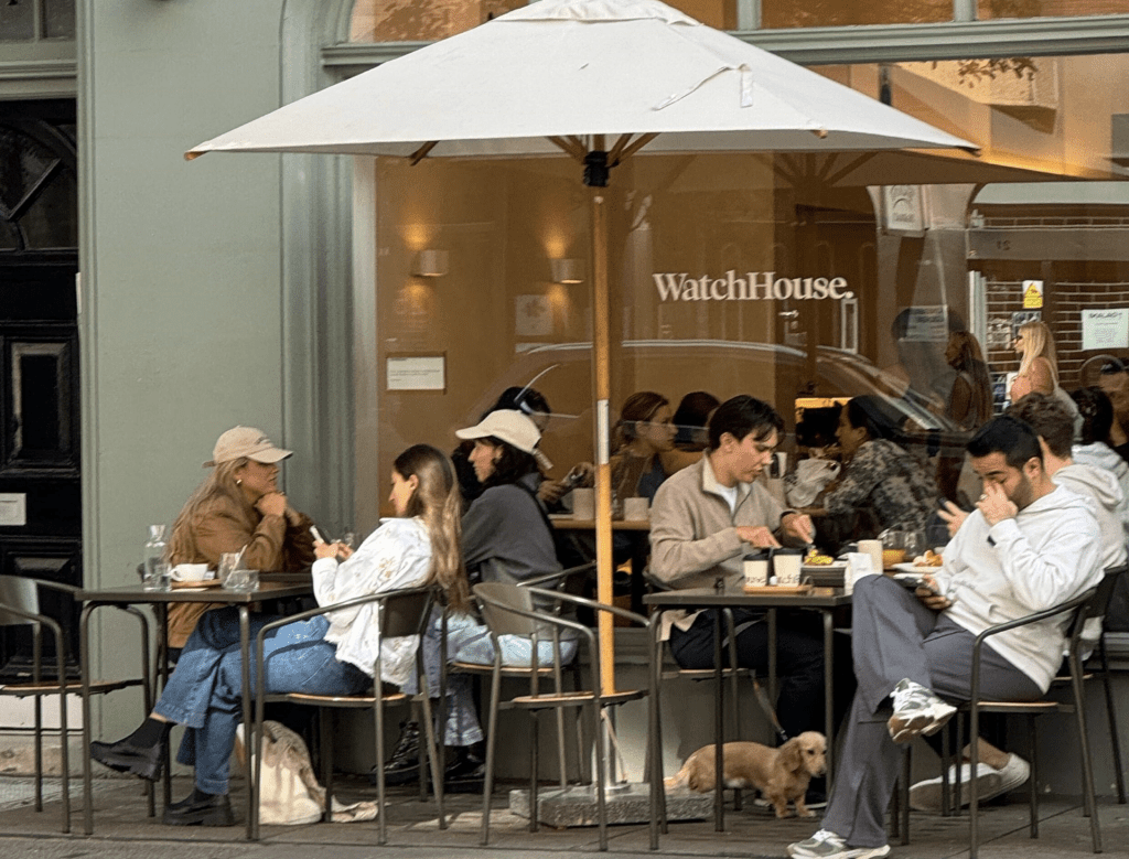 People sitting at dining tables in front of a cafe.