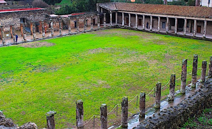Central field surrounded by the remains of the Gladiator Barracks structure and columns in the Pompeii Archaeological Park.