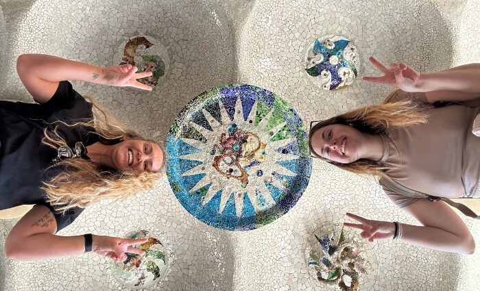 Two travelers posing beneath the mosaic ceiling medallions in the Hypostyle Room at Park Guell